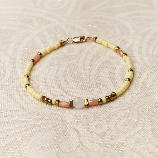 Bracelet of light yellow glass beads with a pink gemstone in the center on a cream background.