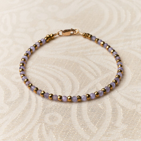 Bracelet with lilac and gold stones. Lying on a cream background.