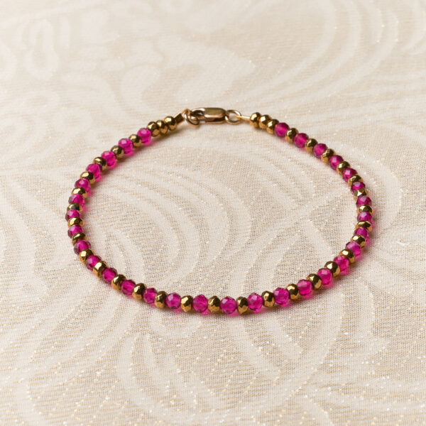 Bracelet with fuchsia and gold stones. Lying on a cream background.
