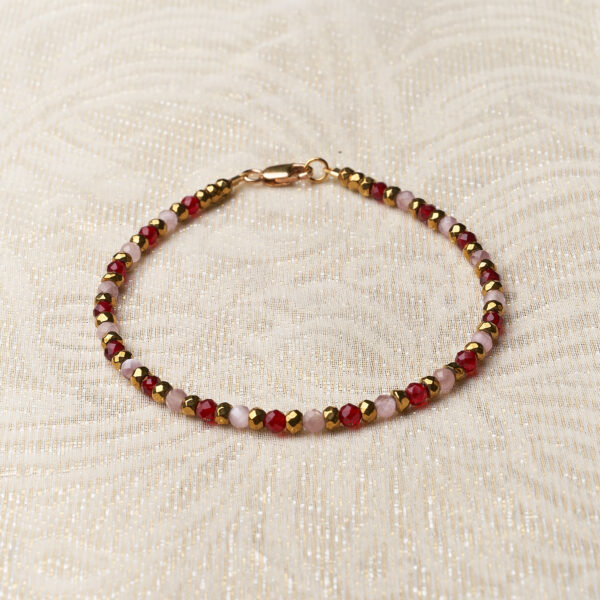Bracelet with alternating pink/red and gold colored stones. Lying on a cream background.